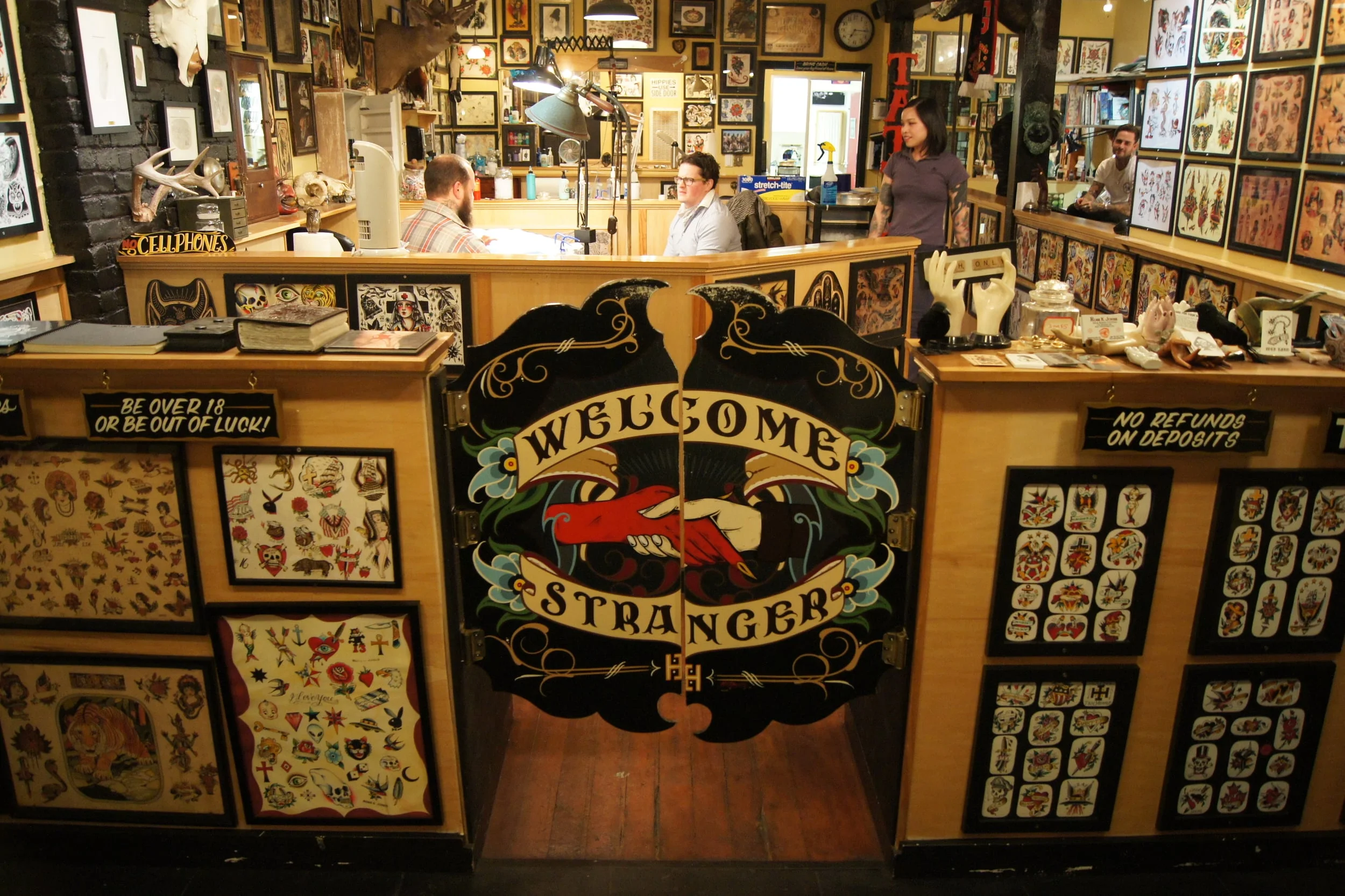 Idle Hand Tattoo front counter with Welcome Stranger gate and flash art covering every surface
